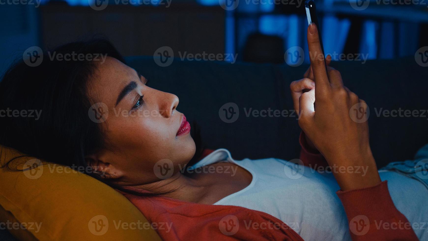 aziatische dame gebruikt telefoon slaap in bed thuis voel me saai en scrollen controleren telefoon zie bericht online. foto