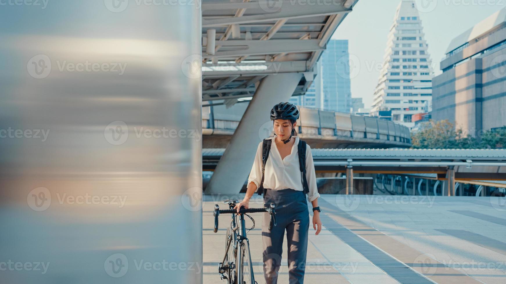 aziatische zakenvrouw gaat aan het werk op kantoor lopen en glimlachen draag rugzak kijk rond neem de fiets op straat rond het bouwen aan een stadsstraat. fiets woon-werkverkeer, woon-werkverkeer op de fiets, zakelijke forens concept. foto