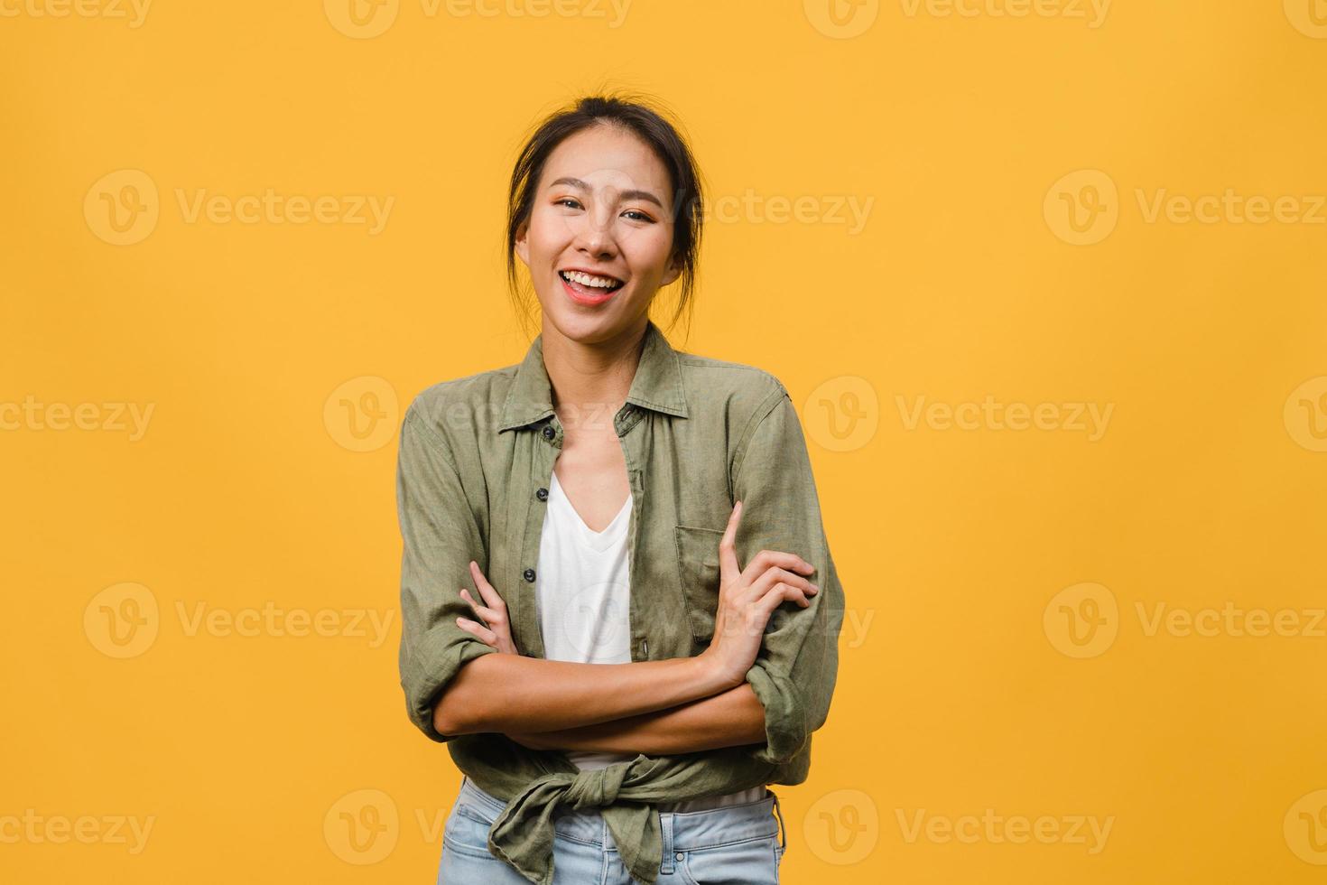 portret van jonge Aziatische dame met positieve uitdrukking, armen gekruist, breed glimlachen, gekleed in casual kleding en camera kijken over gele achtergrond. gelukkige schattige blije vrouw verheugt zich over succes. foto