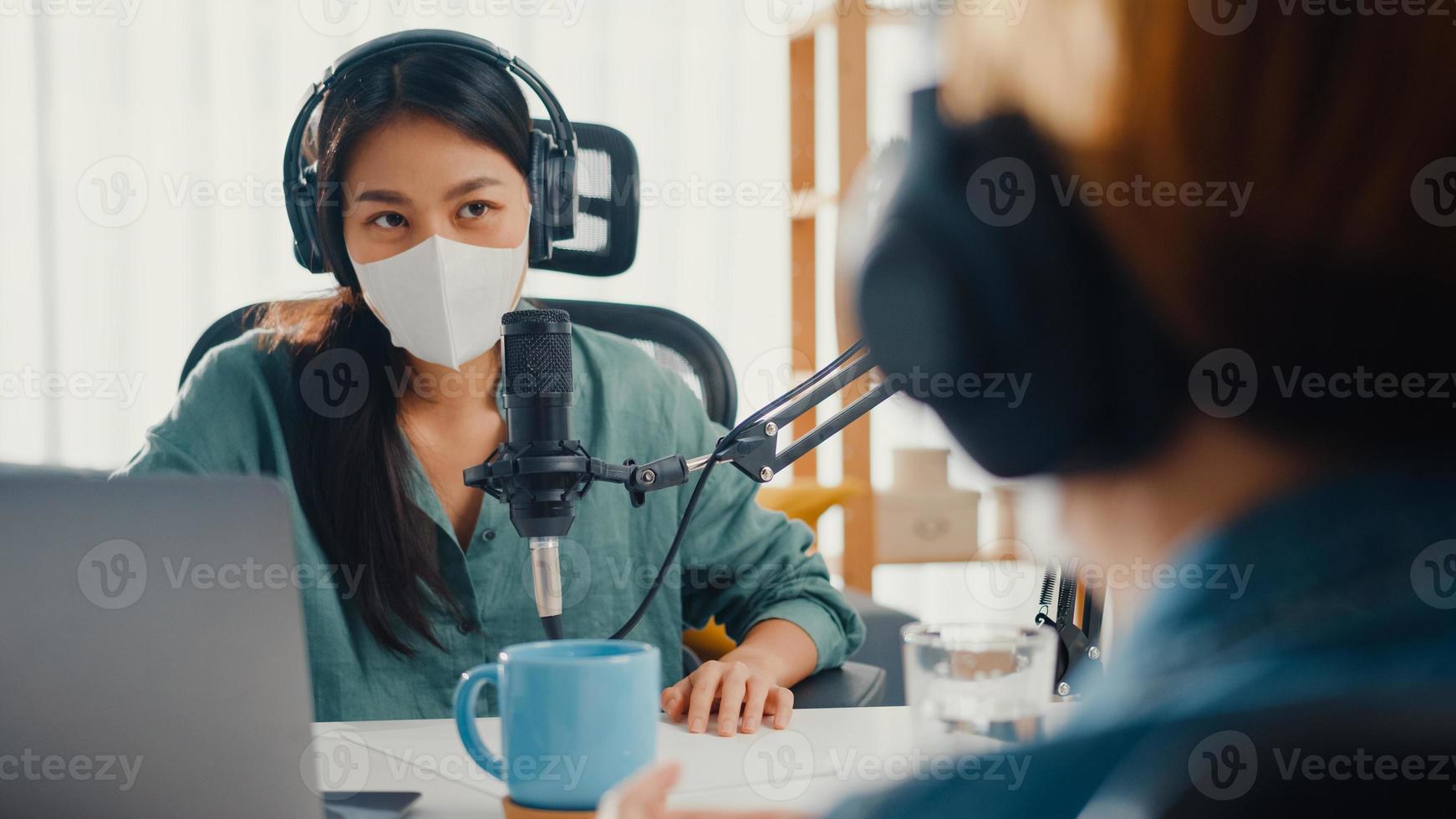 Azië meisje radio-host record podcast gebruik microfoon draag hoofdtelefoon interview gast inhoud draag masker bescherm virus gesprek praten en luisteren in haar kamer. podcast vanuit huis, coronavirus quarantaine. foto