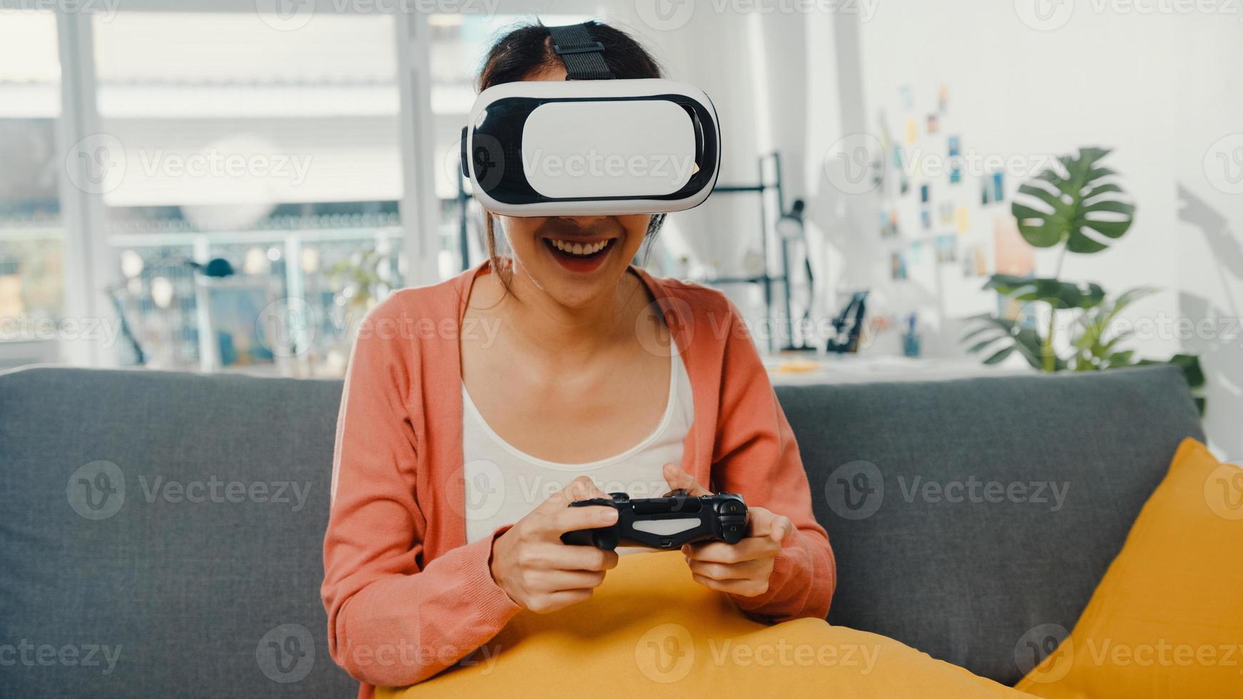 aziatische dame draagt een headsetbril met virtual reality en speelt joystickspel op de bank in de woonkamer in huis. blijf thuis covid quarantaine, stel de realiteit opnieuw voor, vr thuis, vr-technologie van toekomstig concept. foto