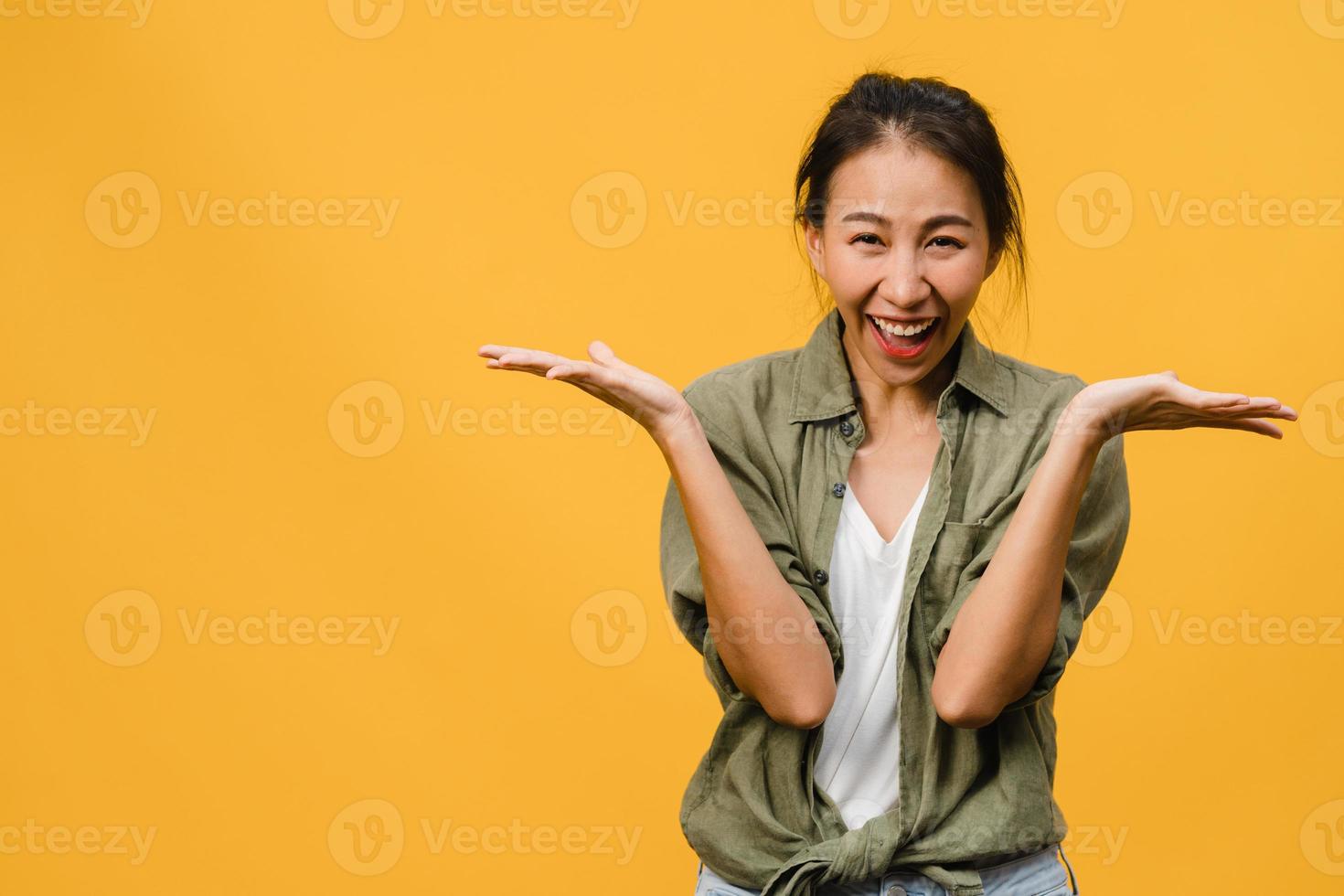 jonge Aziatische dame voelt geluk met positieve uitdrukking, vrolijke verrassing funky, gekleed in casual doek en kijkend naar camera geïsoleerd op gele achtergrond. gelukkige schattige blije vrouw verheugt zich over succes. foto