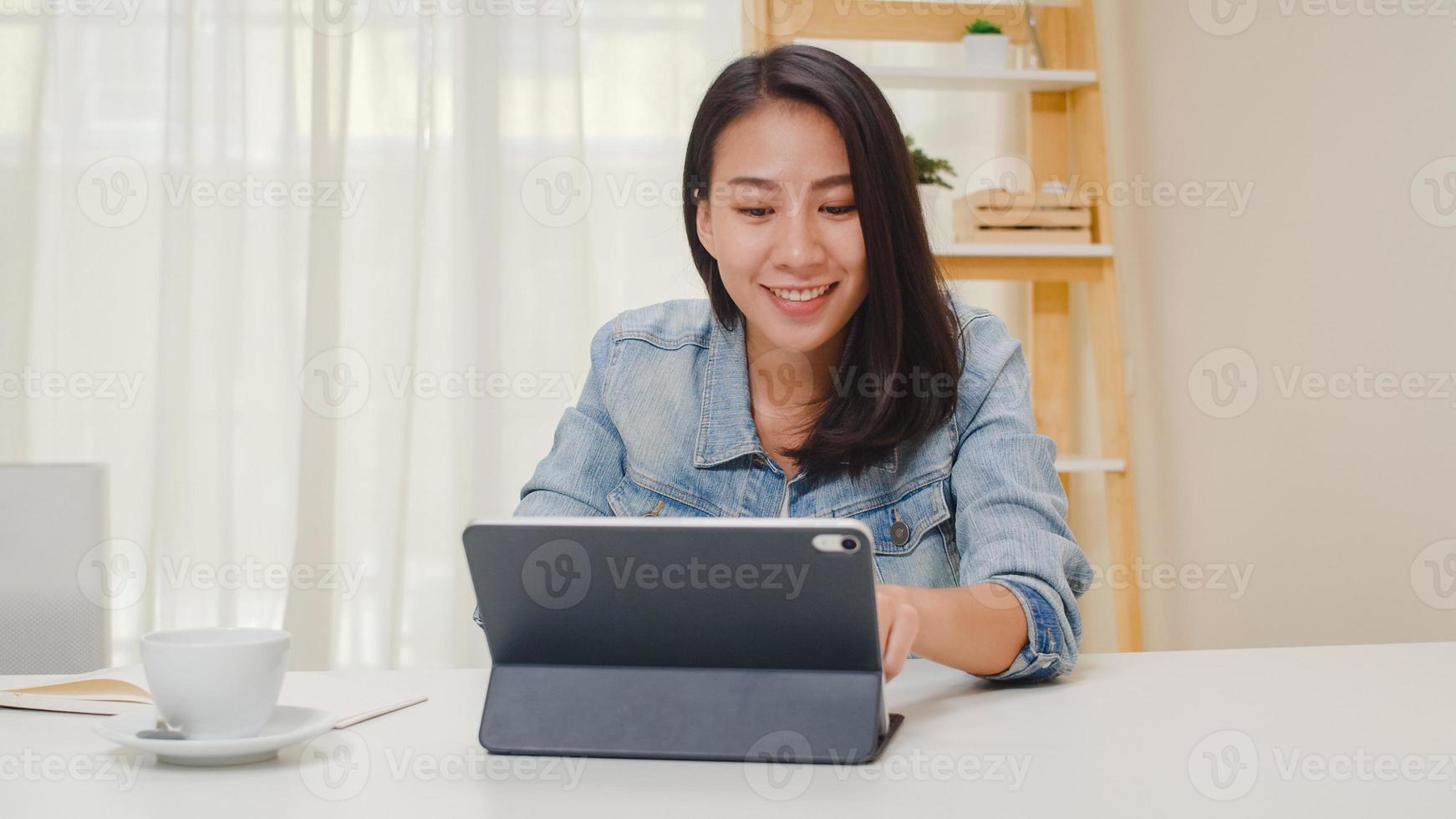 portret van freelance slimme zakelijke vrouwen vrijetijdskleding met behulp van tablet werken op de werkplek in de woonkamer thuis. gelukkig jong Aziatisch meisje ontspannen zittend op bureau zoeken en werk doen op internet. foto
