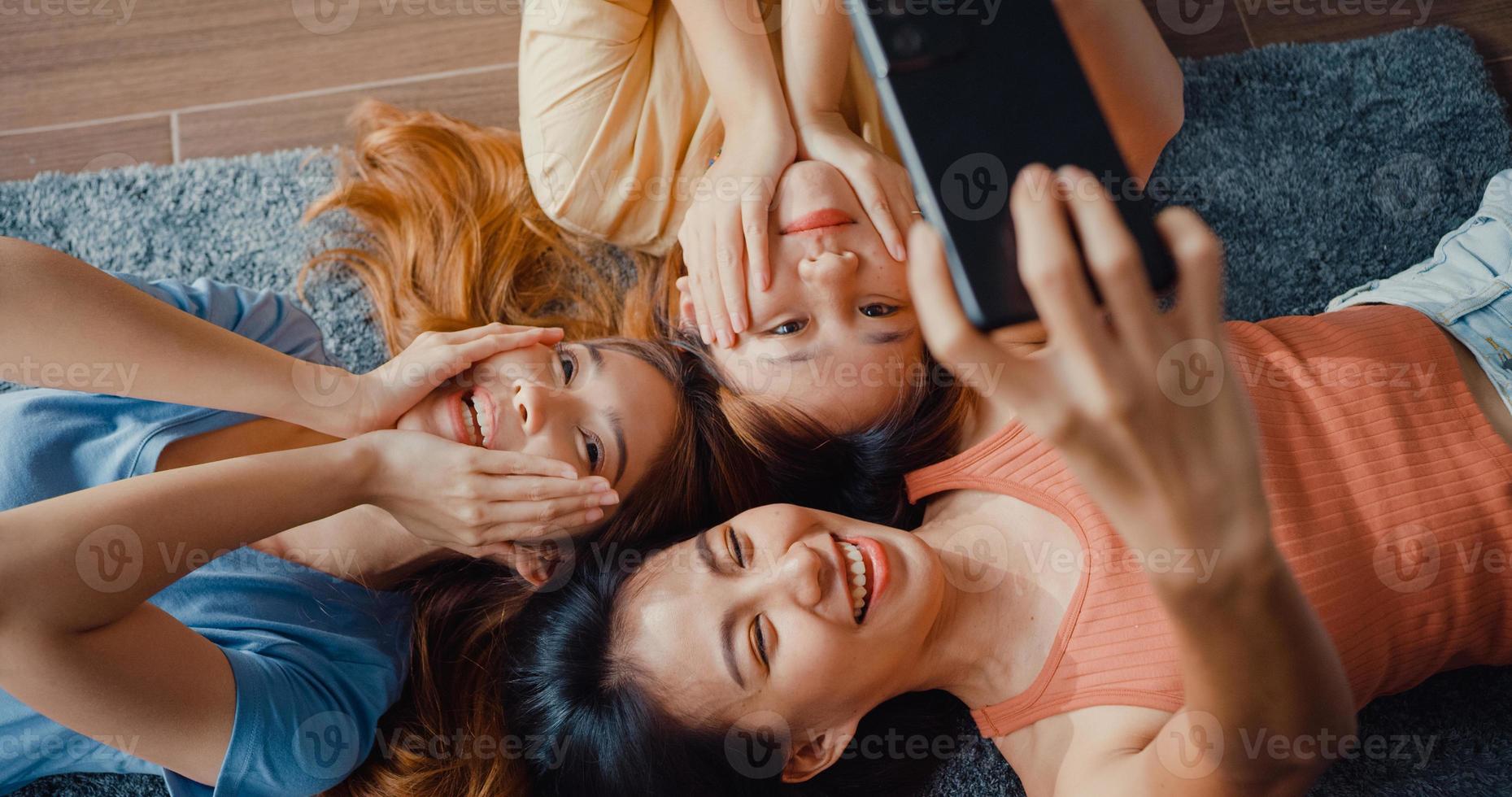 bovenaanzicht close-up groep Azië dames met geluk geniet van moment houd smartphone glimlachend neem herinneringen foto liggend op tapijt in de vloer woonkamer thuis. levensstijl activiteit quarantaine concept.