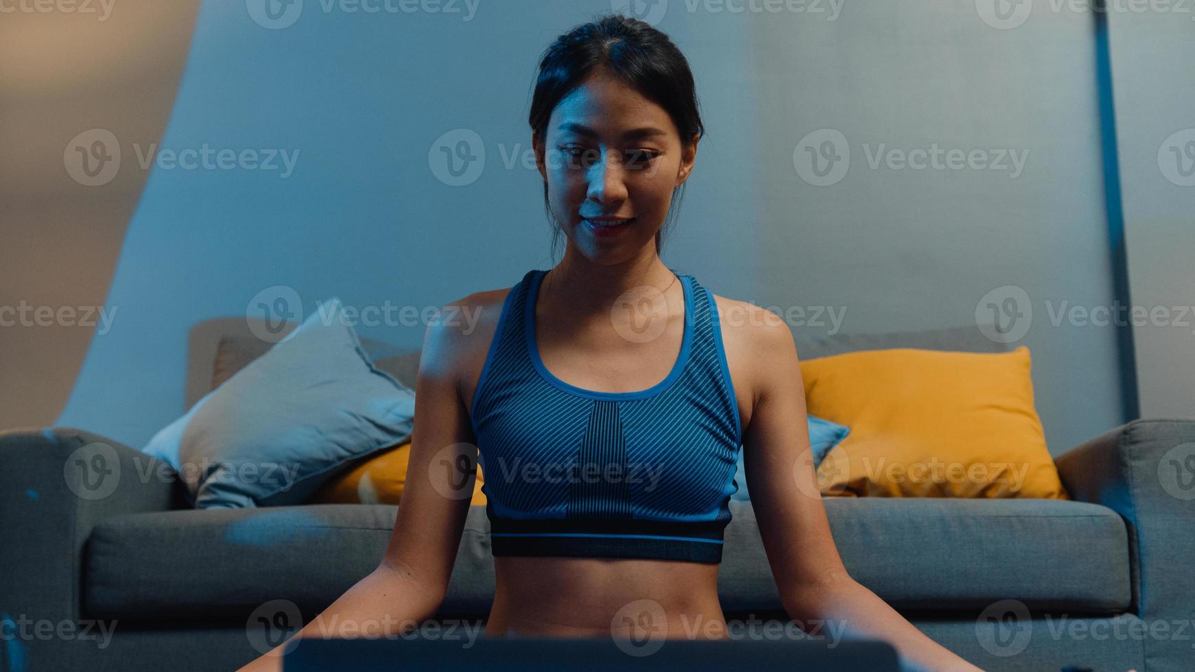 jonge aziatische dame in sportkledingoefeningen die aan het trainen zijn en laptop gebruiken om thuis een yogavideo-tutorial te bekijken. afstandstraining met personal trainer, sociale afstand, online onderwijsconcept. foto