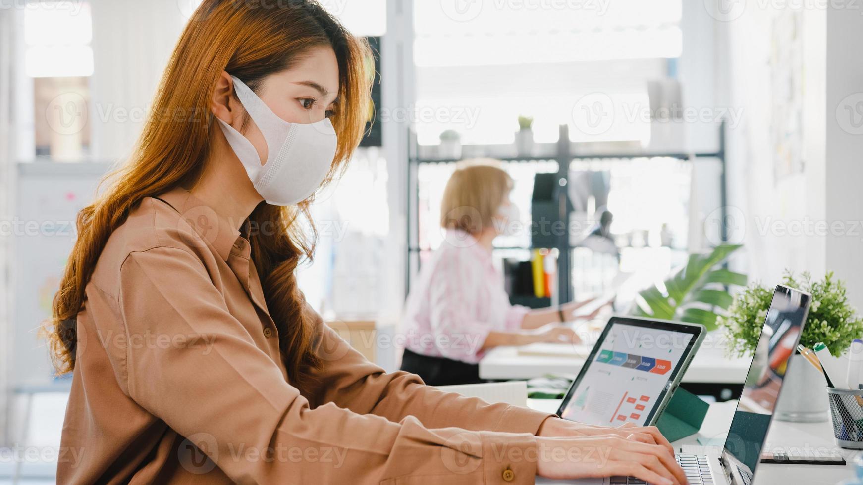 azië zakenvrouw ondernemer met medisch gezichtsmasker voor sociale afstand in nieuwe normale situatie voor viruspreventie tijdens het gebruik van laptop terug op het werk op kantoor. levensstijl na het coronavirus. foto