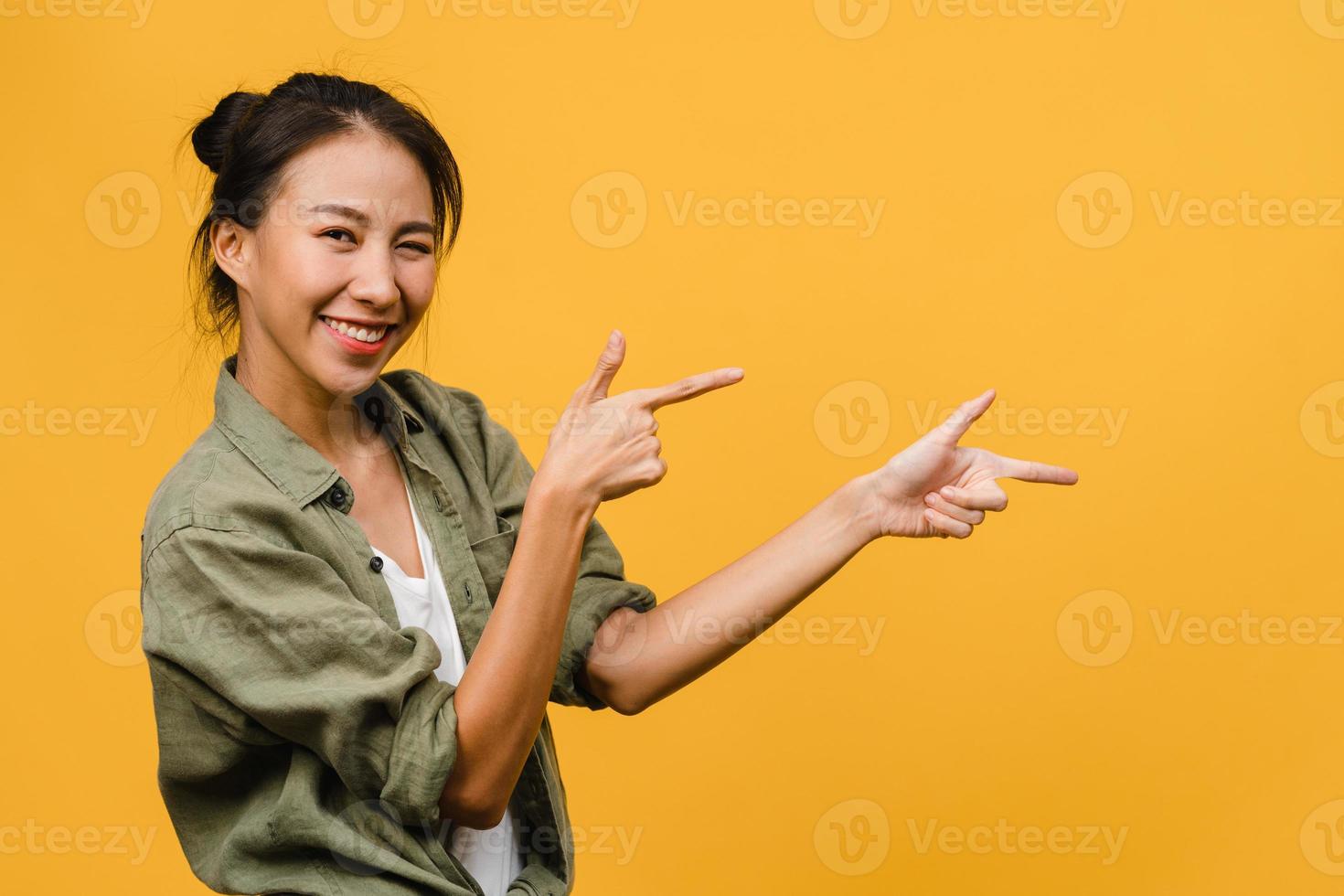 portret van een jonge aziatische dame die lacht met een vrolijke uitdrukking, laat iets geweldigs zien op lege ruimte in casual doek en kijkt naar camera geïsoleerd over gele achtergrond. gezichtsuitdrukking concept. foto