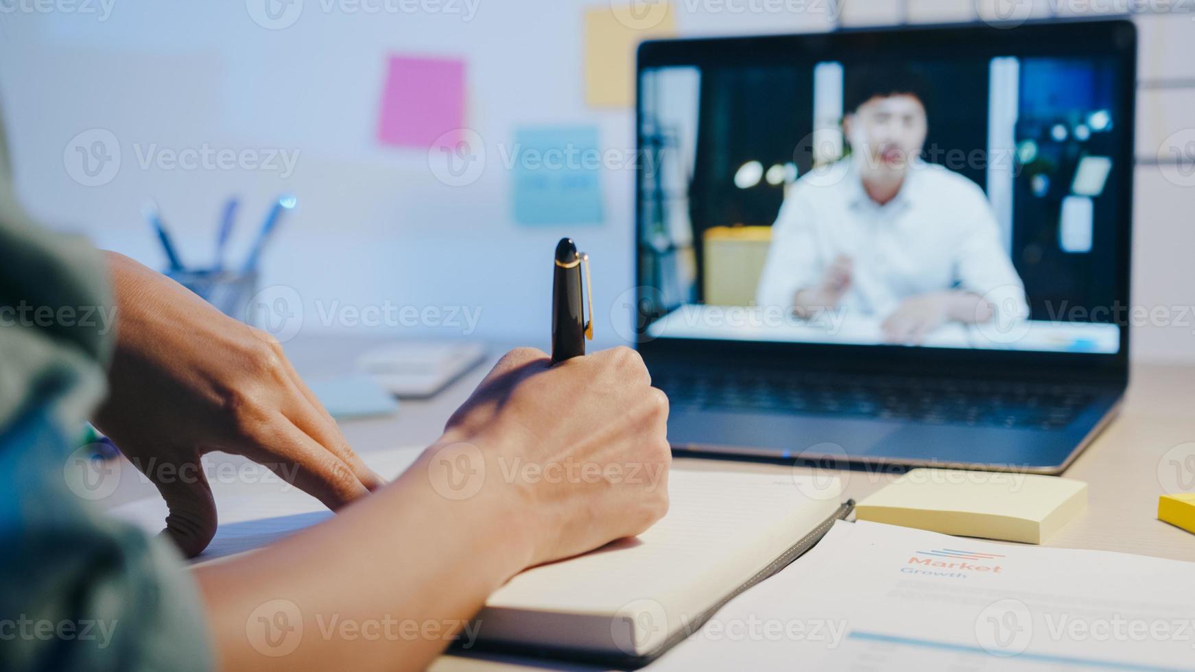 azië zakenvrouw met behulp van laptop praten met collega's over plan in videogesprek vergadering in woonkamer. 's nachts thuiswerken, werken op afstand, sociale afstand, quarantaine voor coronavirus. foto