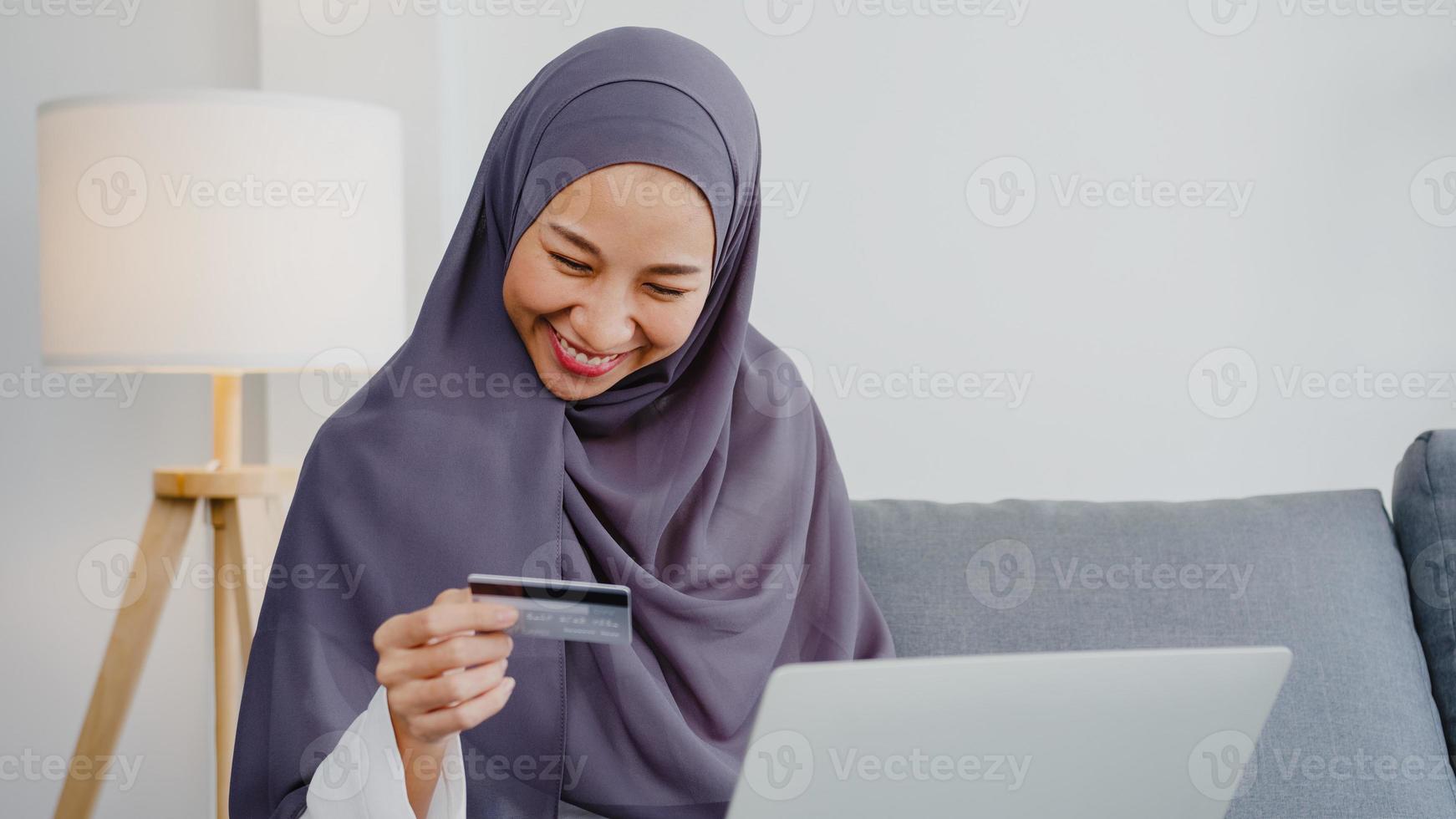 azië moslimdame met behulp van laptop, creditcard kopen en kopen e-commerce internet in de woonkamer thuis. thuis blijven, online winkelen, zelfisolatie, sociale afstand, quarantaine voor coronavirus. foto