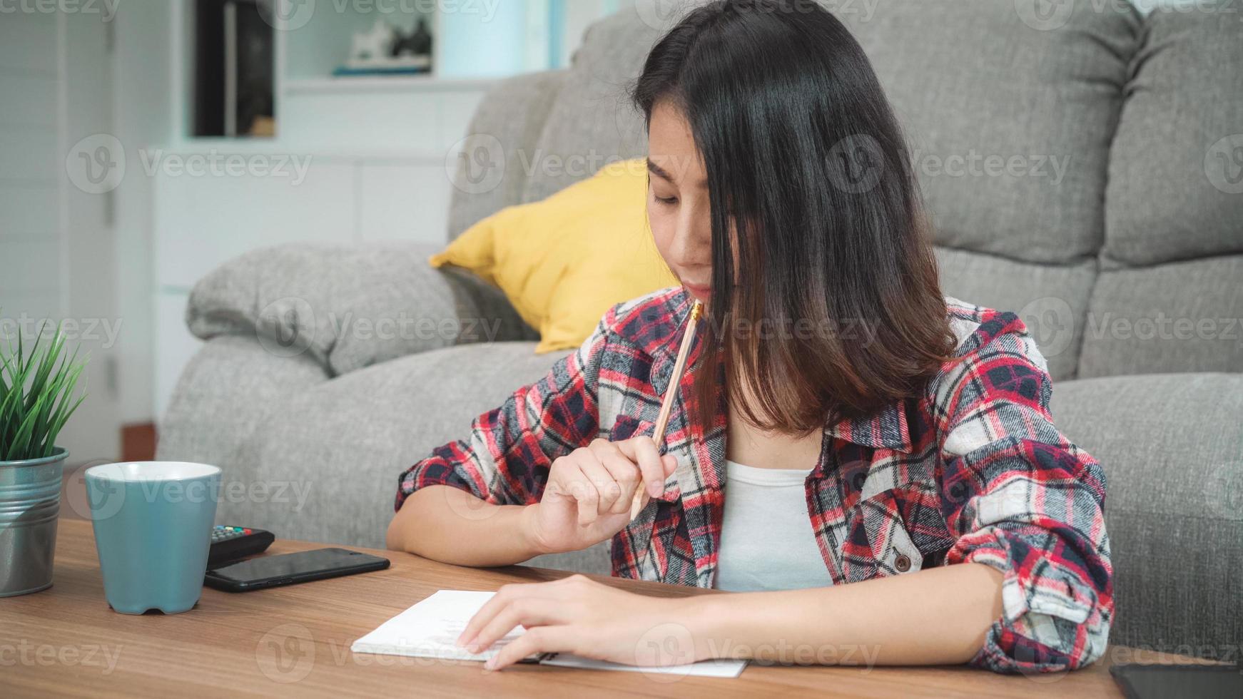 aziatische studentenvrouw doet thuis huiswerk, vrouw gebruikt tablet om thuis op de bank in de woonkamer te zoeken. levensstijl vrouwen ontspannen thuis concept. foto