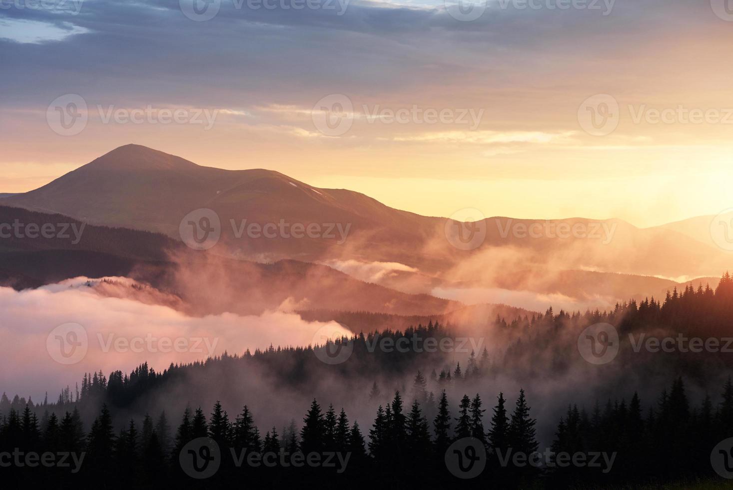 prachtige zonsondergang in de bergen. landschap met zonlicht schijnt door oranje wolken en mist foto