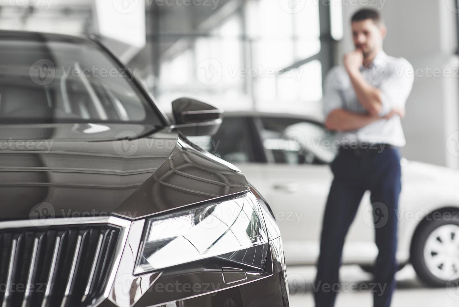 knappe jonge man consultant bij auto salon staande in de buurt van auto. foto