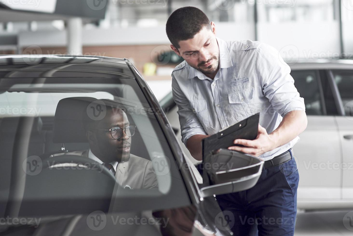 een Afrikaanse man die een nieuwe auto koopt, controleert een auto terwijl hij met een professionele verkoper praat. foto