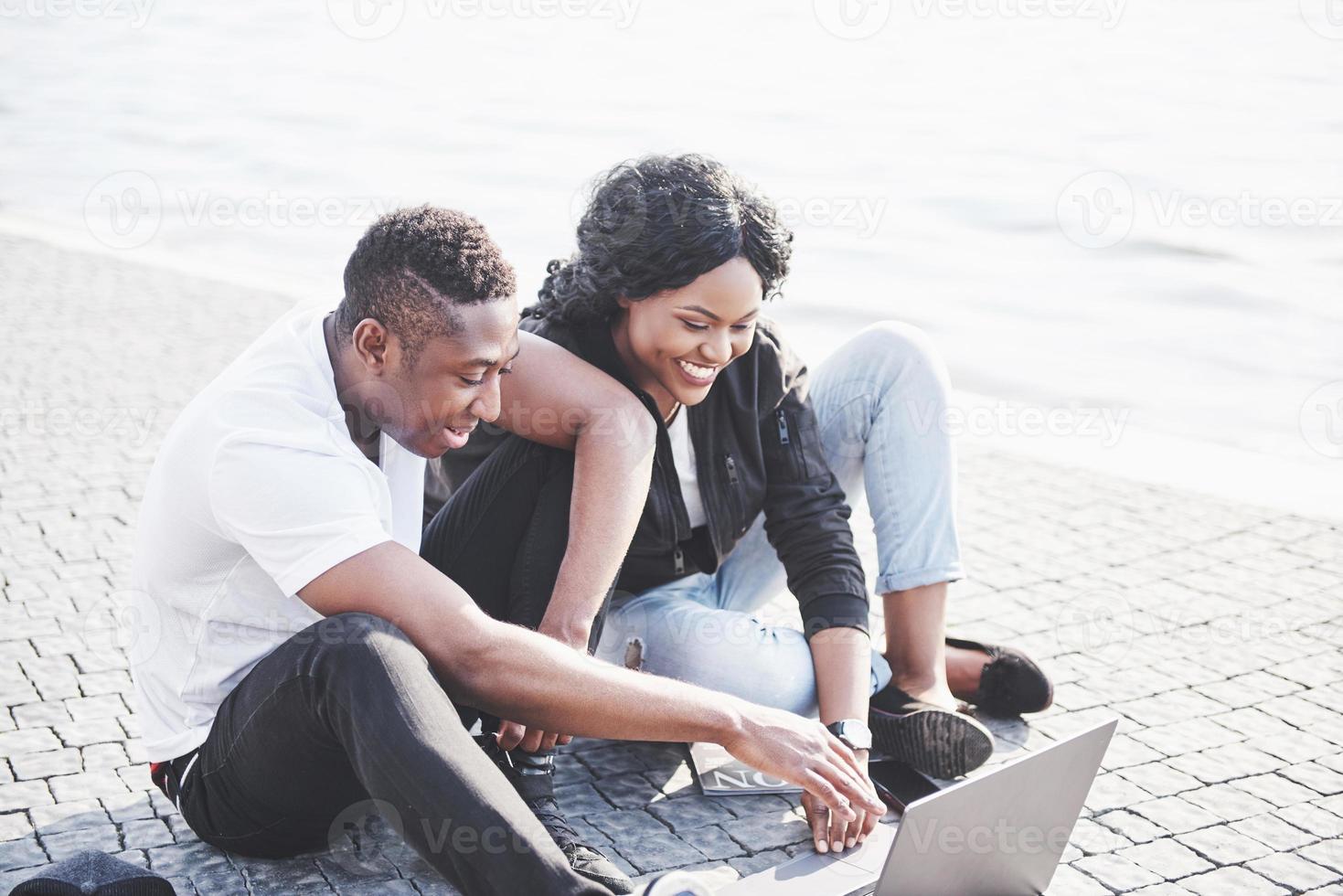twee gelukkige vrienden van studenten of zakenpartners zitten buiten en genieten van een laptop foto
