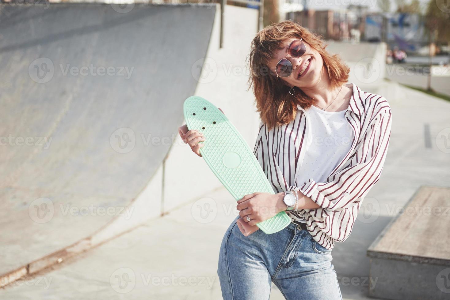 stijlvolle mooie jonge vrouw met een skateboard, op een mooie zonnige zomerdag. foto