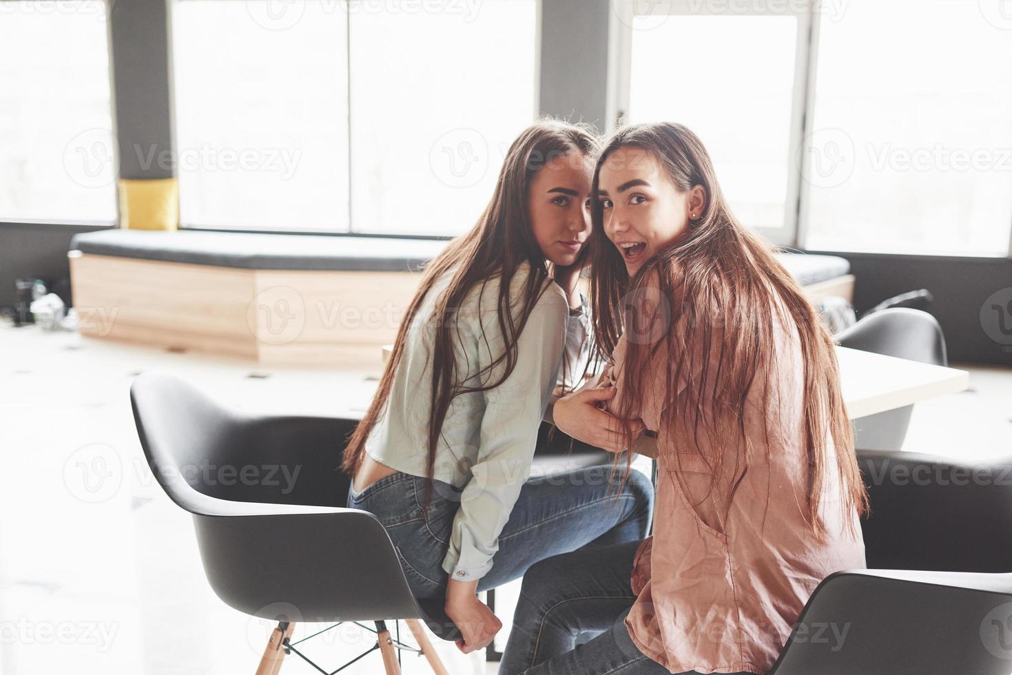 twee mooie tweelingmeisjes brengen tijd door. zussen ontspannen in een café en samen plezier maken en fluisteren foto