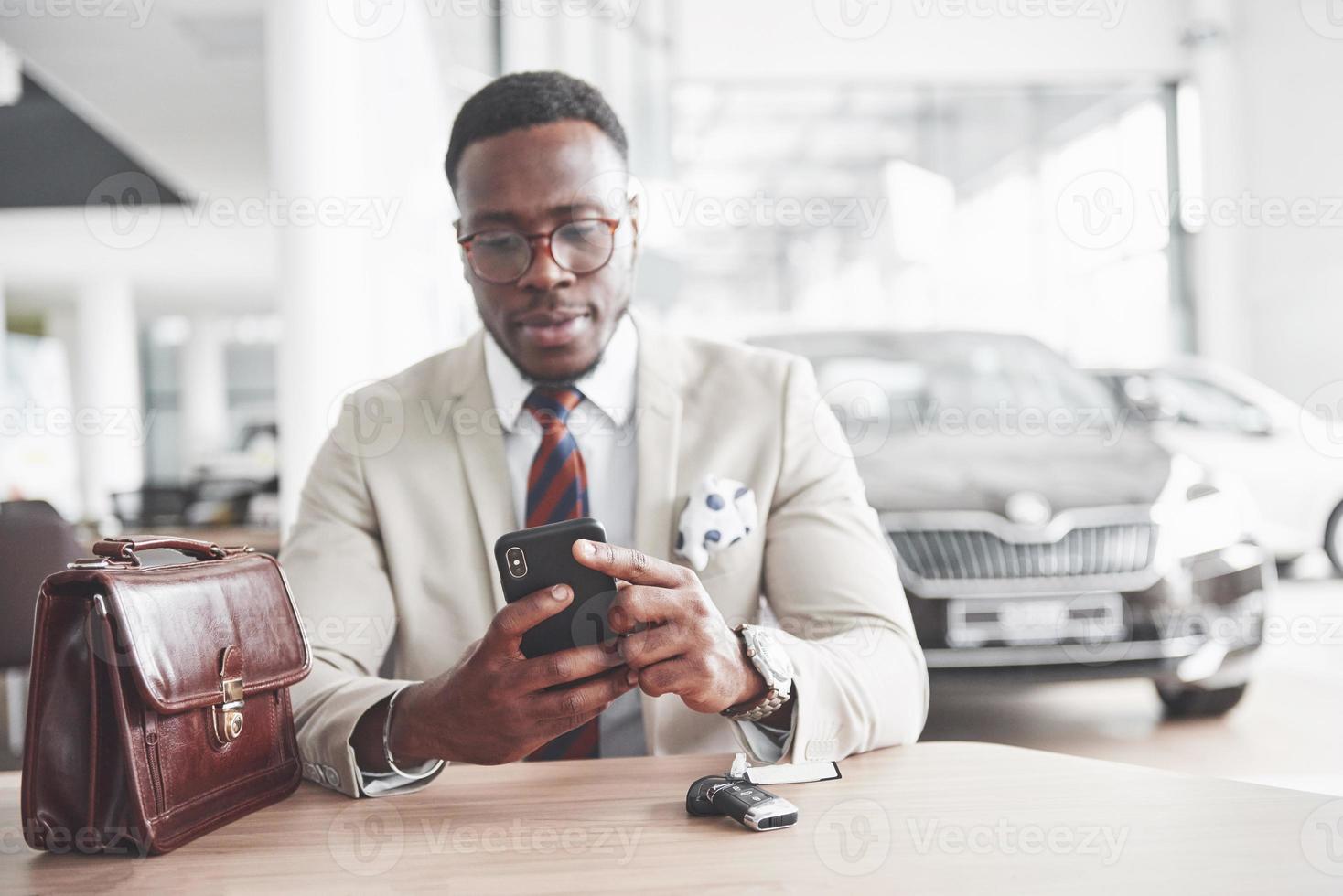 aantrekkelijke zwarte zakenman zit aan de tafel bij de autodealer, hij tekent een contract en koopt een nieuwe auto foto