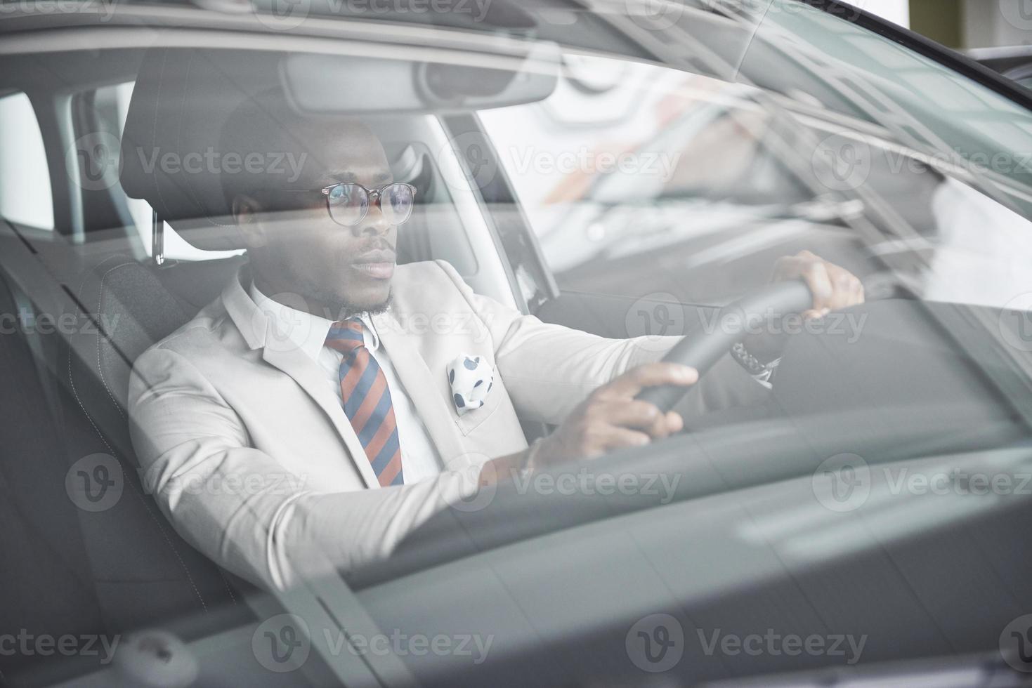 vooraanzicht van knappe Afrikaanse elegante serieuze zakenman rijdt in een auto foto