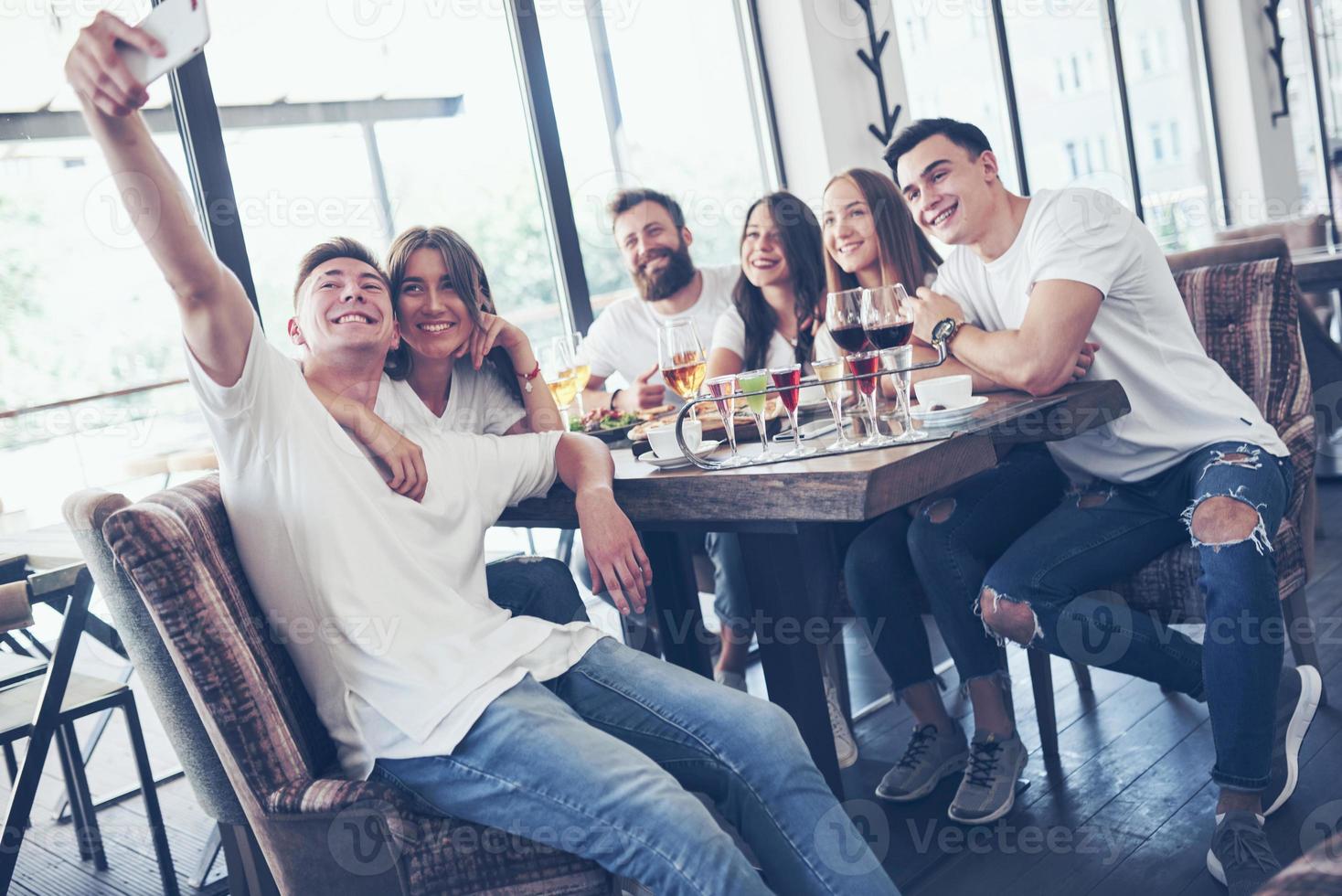 een groep mensen maakt een selfie-foto in een café. de beste vrienden verzamelden zich aan een eettafel, aten pizza en zongen verschillende drankjes foto