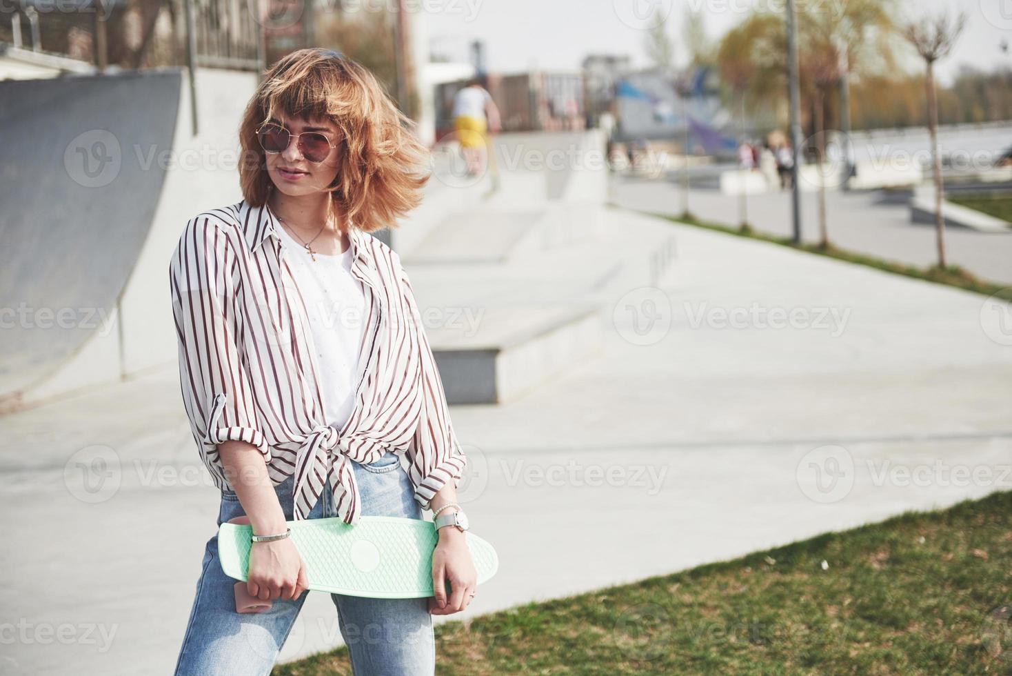 stijlvolle mooie jonge vrouw met een skateboard, op een mooie zonnige zomerdag. foto