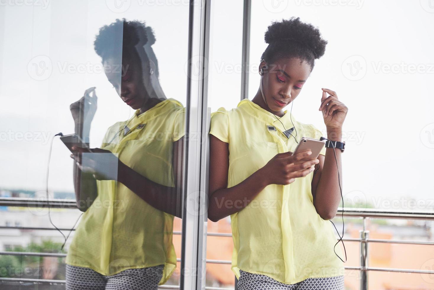 portret van aantrekkelijke jonge zwarte vrouw met mobiele telefoon en koptelefoon tijdens het luisteren naar muziek foto