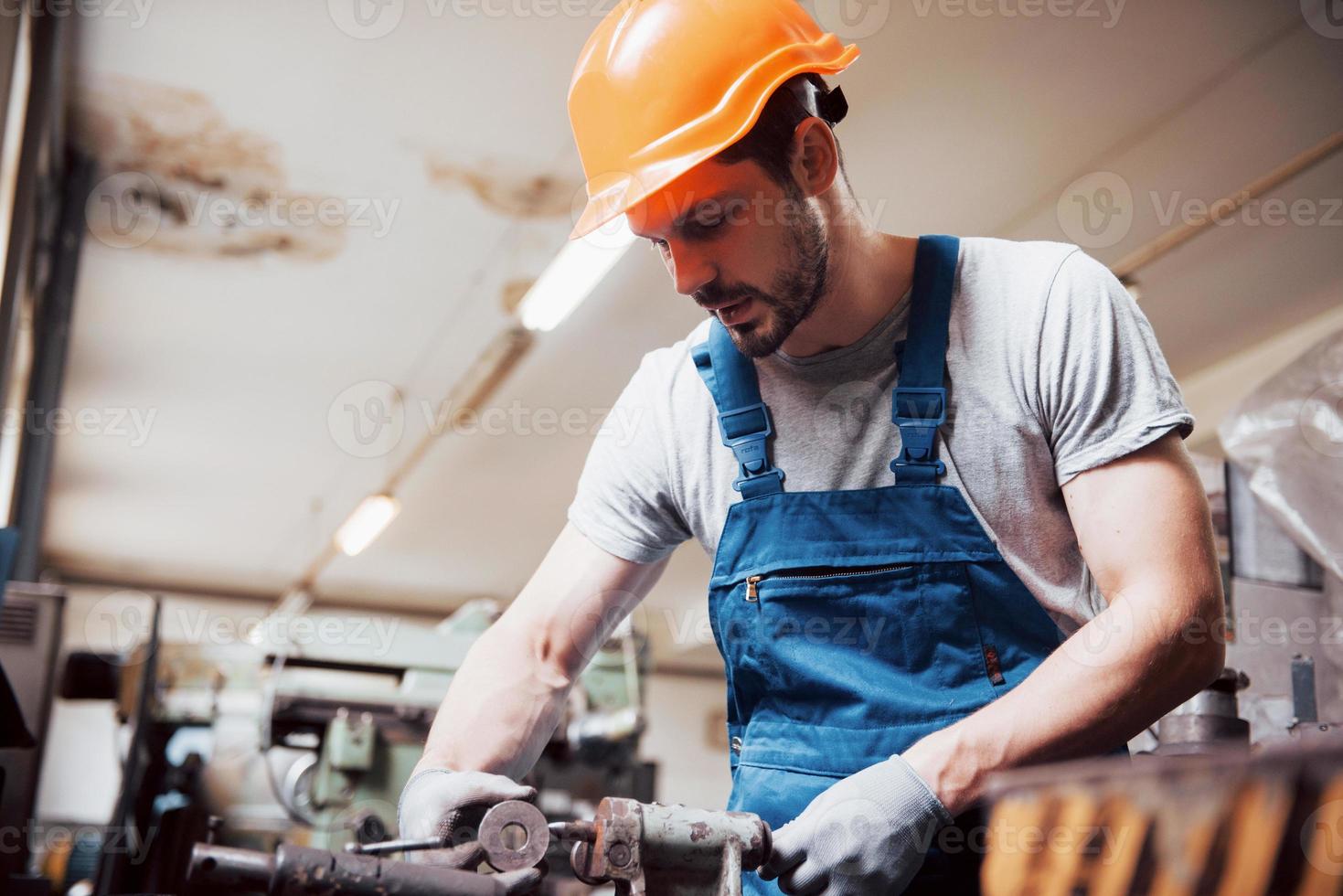 portret van een jonge arbeider met een helm in een grote metaalbewerkingsfabriek. de ingenieur bedient de machines en maakt onderdelen voor gasapparatuur foto