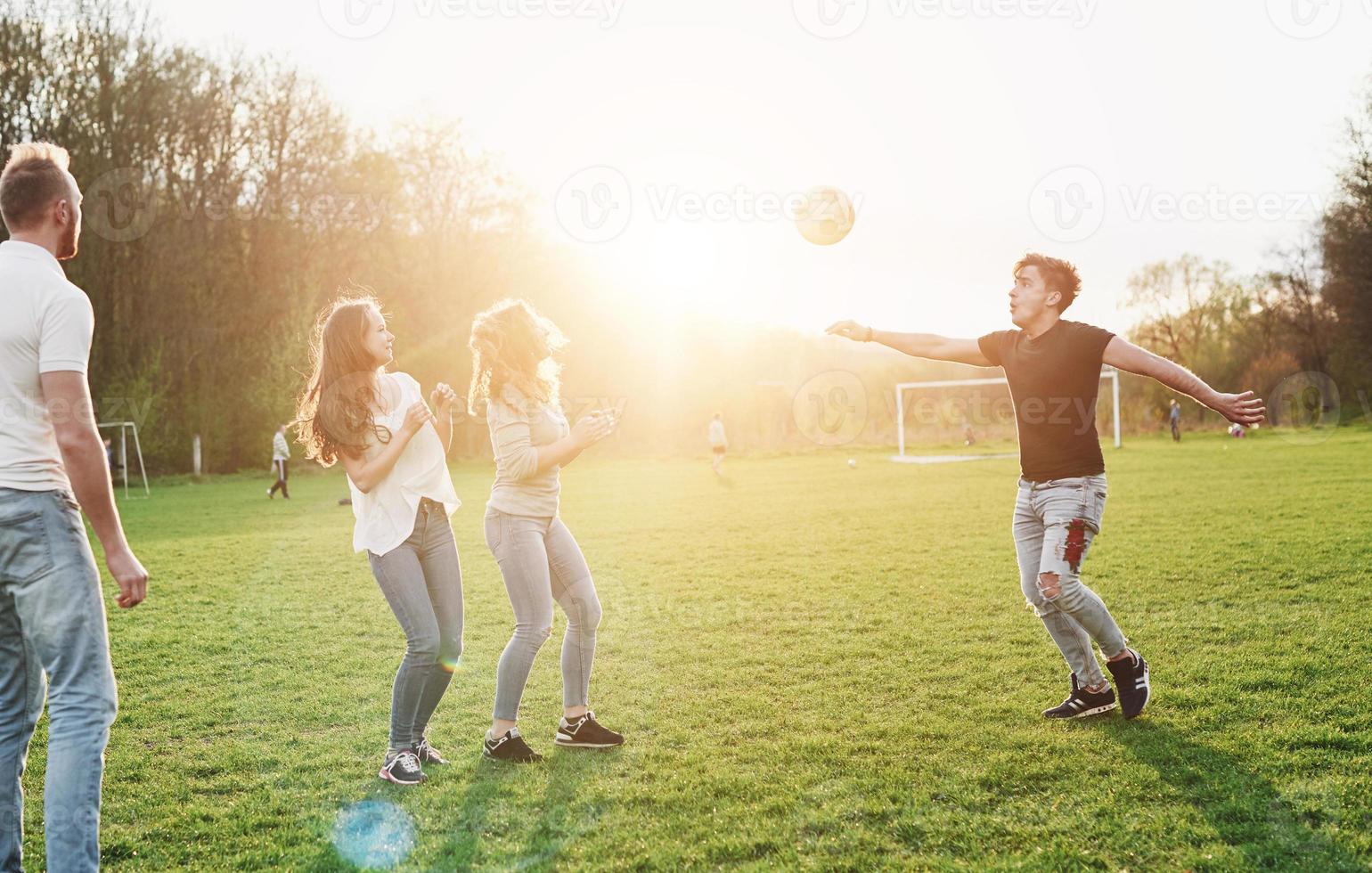 een groep vrienden in casual outfit voetballen in de open lucht. mensen veel plezier en plezier. actieve rust en schilderachtige zonsondergang. foto