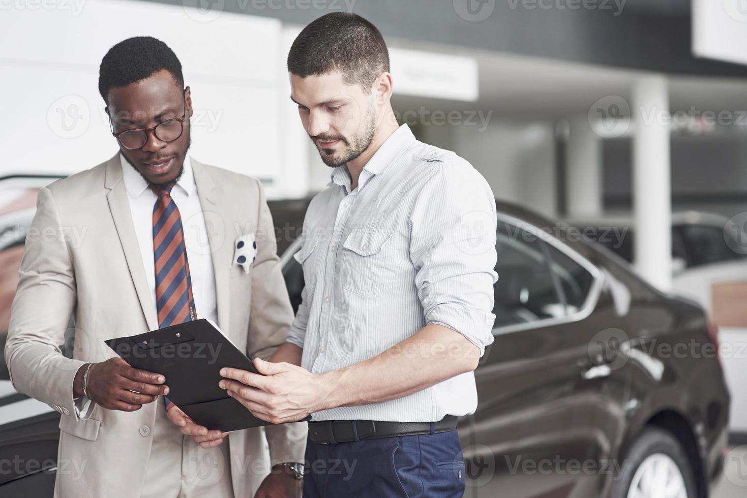 een Afro-Amerikaan met een adviseur bij een autodealer kiest een auto. goed koopje. foto