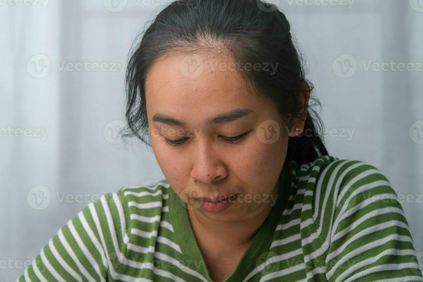 verveeld vrouw zittend Bij bureau Bij huis. Aziatisch vrouw wie is verveeld, moe en behoeften een kom tot rust dag. foto