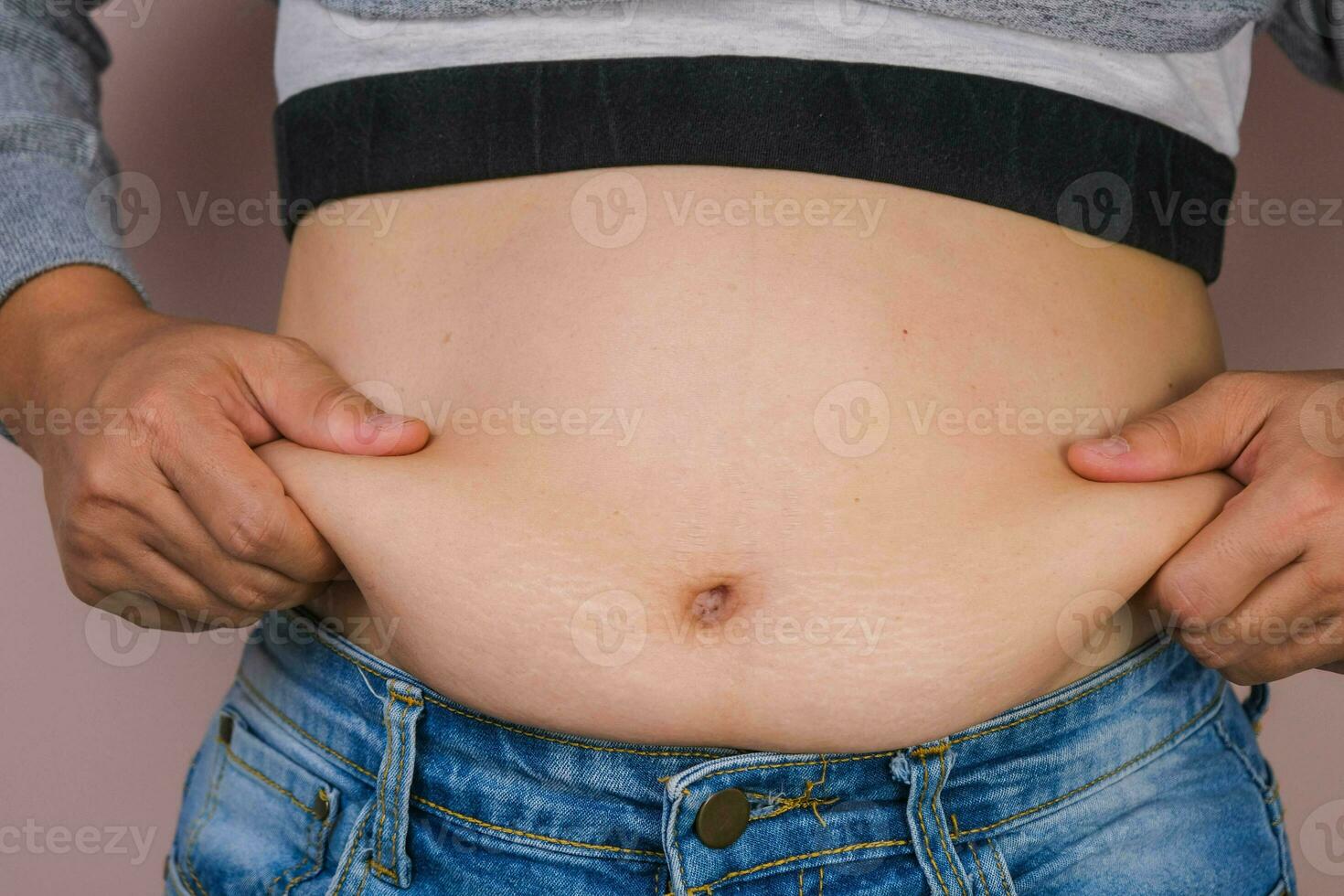 dik vrouw hand- Holding buitensporig buik dik geïsoleerd Aan roze achtergrond. te zwaar vettig buik van vrouw. vrouw eetpatroon en lichaam Gezondheid zorg concept foto