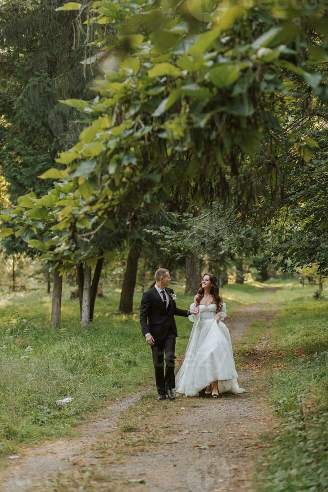 de bruid en bruidegom houden handen, wandelen in de tuin op zoek Bij elk andere foto