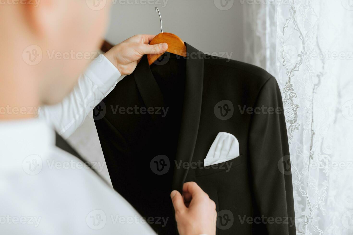 een jong Mens houdt zijn zwart jasje Aan een hanger in zijn handen. de bruidegom is voorbereidingen treffen voor de bruiloft ceremonie. gedetailleerd detailopname foto van handen