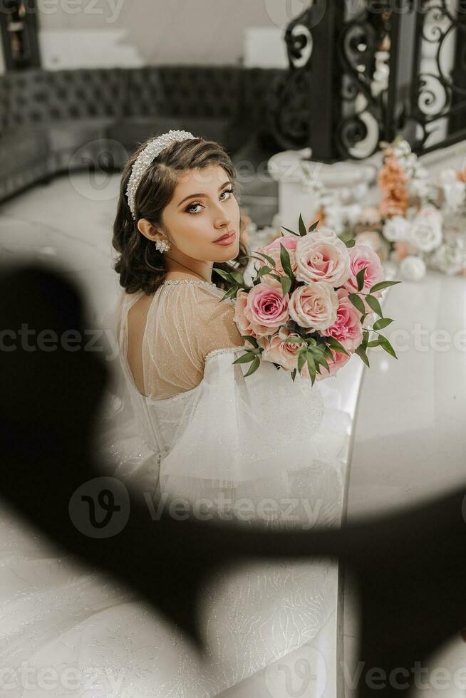 portret van een jong meisje van de rug, met mooi haar- en bedenken in een luxueus bruiloft jurk Aan de stappen van een restaurant in de buurt roos bloemen. verticaal foto. foto