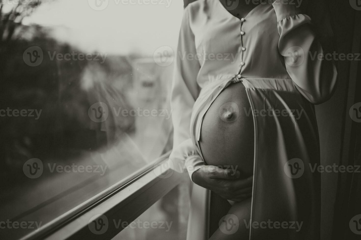 detailopname studio portret van een mooi zwanger jong vrouw door de venster, Holding haar zwanger buik met haar handen. zwart en wit foto