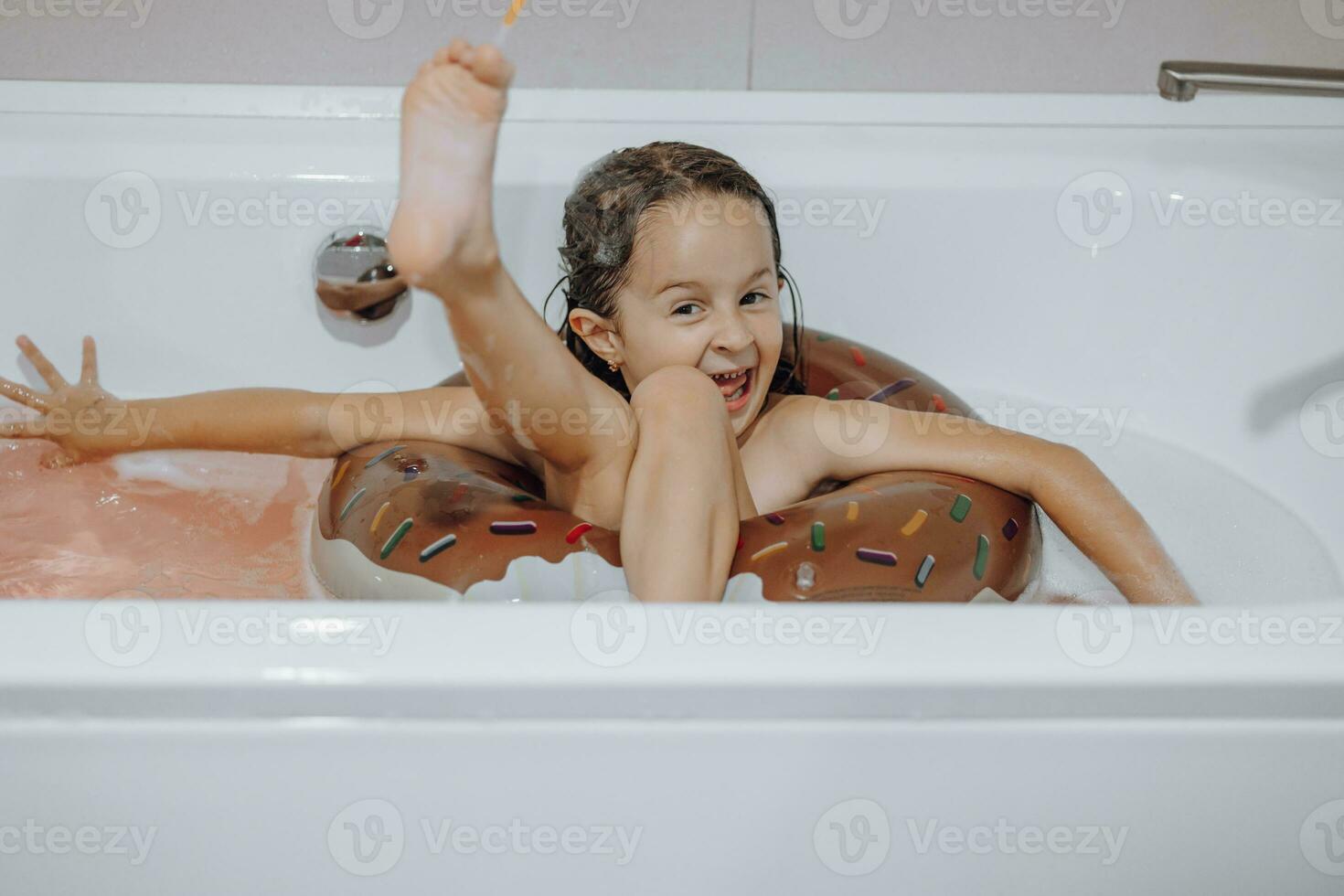 klein, lachend, mooi donker haar meisje met lang haar, kind baadt, wast in een wit bad met schuim. pret foto. foto