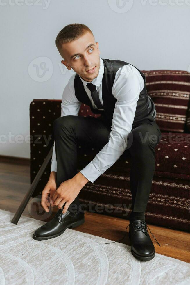 portret. een Mens in een wit shirt, hesje en zwart broek is zittend Aan een sofa en vervelend elegant schoenen. een elegant horloge. Mannen stijl. mode. bedrijf foto