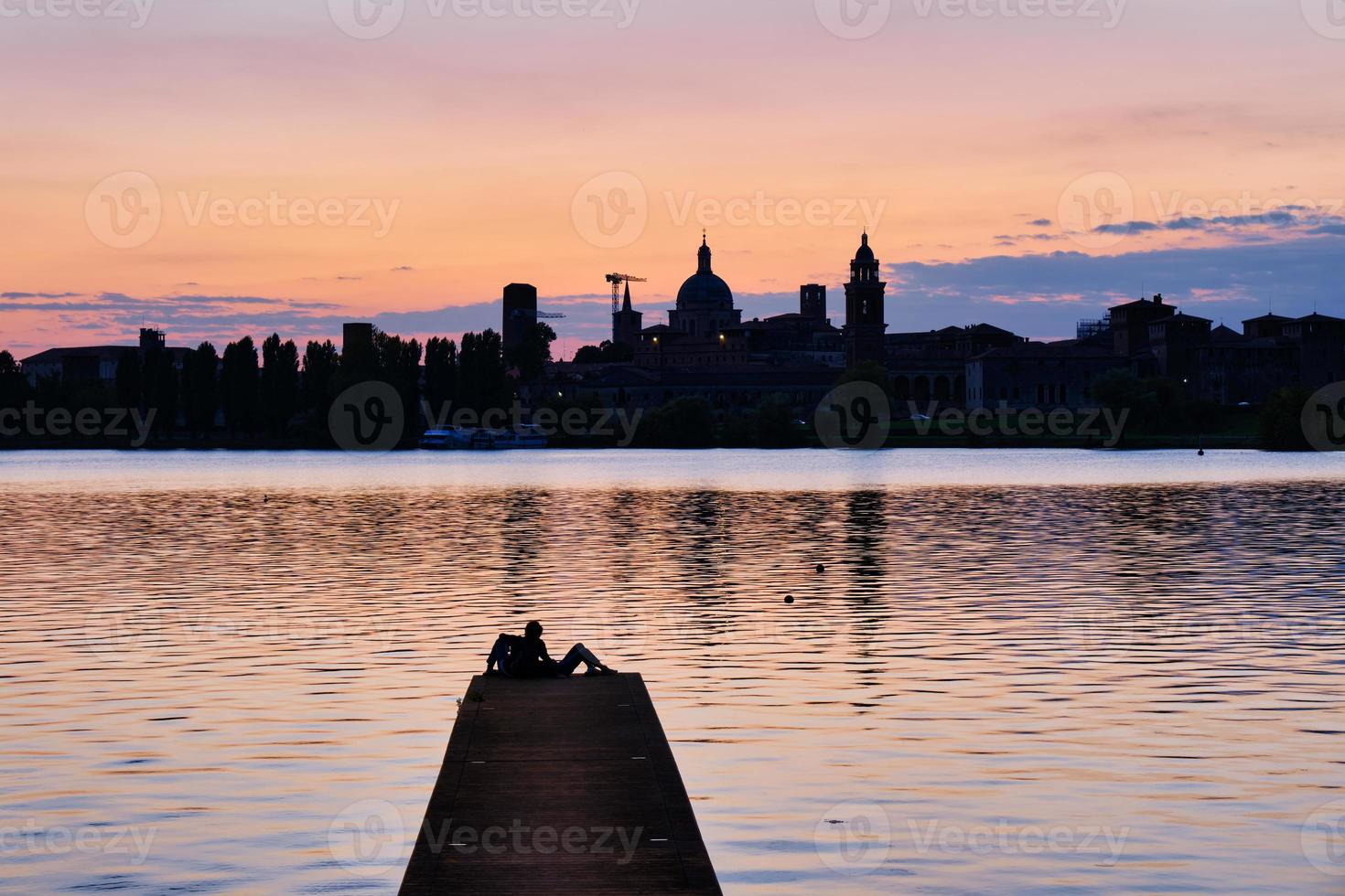 paar zittend op de pier kijkend naar de zonsondergang en de skyline van de stad foto