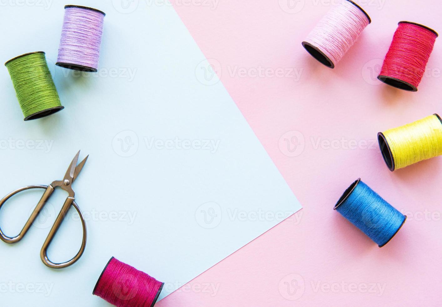 plat leggen van gekleurde draadrollen en schaar voor het naaien op tweekleurige achtergrond, naai- en handwerkconcept. foto