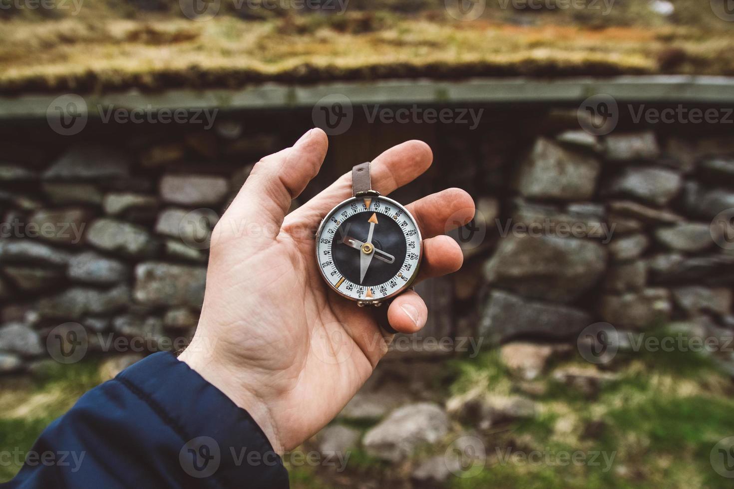 mooie mannenhand houdt een magnetisch kompas vast tegen de achtergrond van huis en bergen rotsen foto