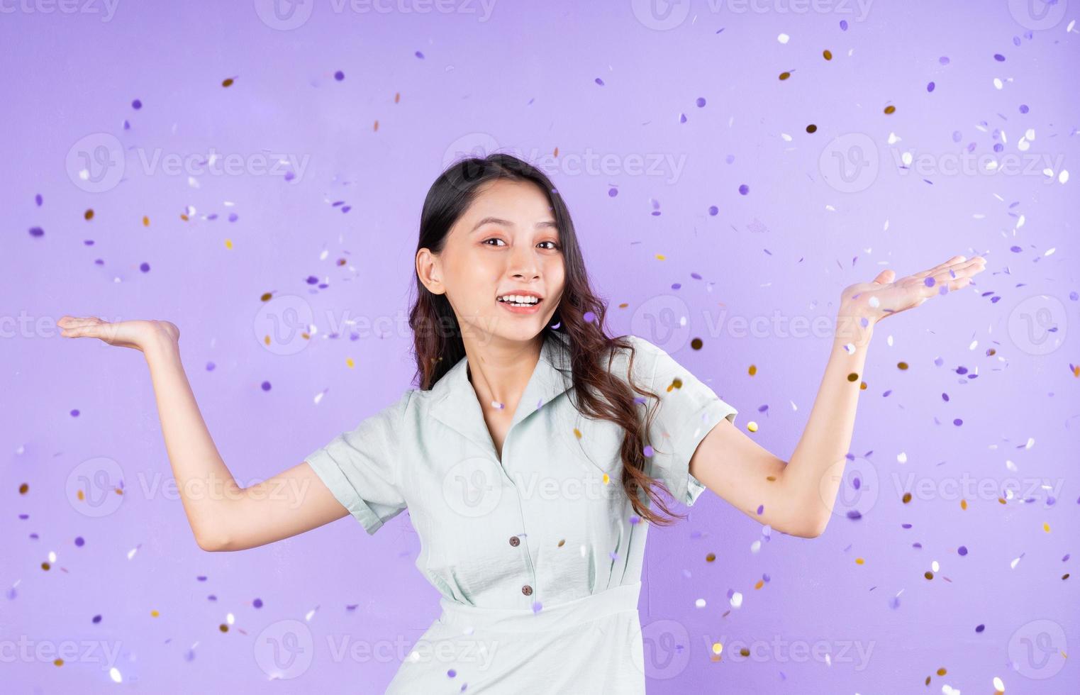 portret van een mooi meisje dat eronder staat en confetti koopt om te vieren, geïsoleerd op een paarse achtergrond foto