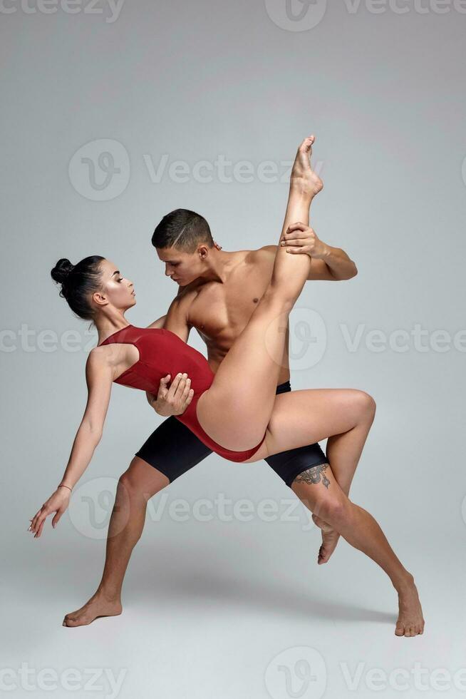 de paar van een atletisch modern ballet dansers zijn poseren tegen een grijs studio achtergrond. foto