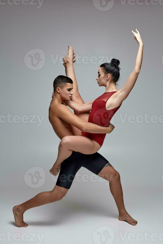 de paar van een atletisch modern ballet dansers zijn poseren tegen een grijs studio achtergrond. foto