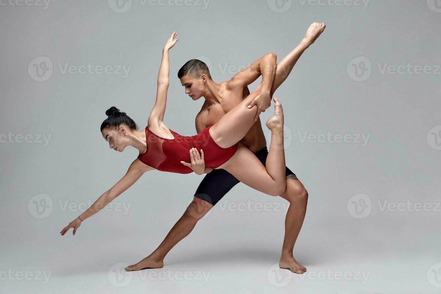 de paar van een atletisch modern ballet dansers zijn poseren tegen een grijs studio achtergrond. foto