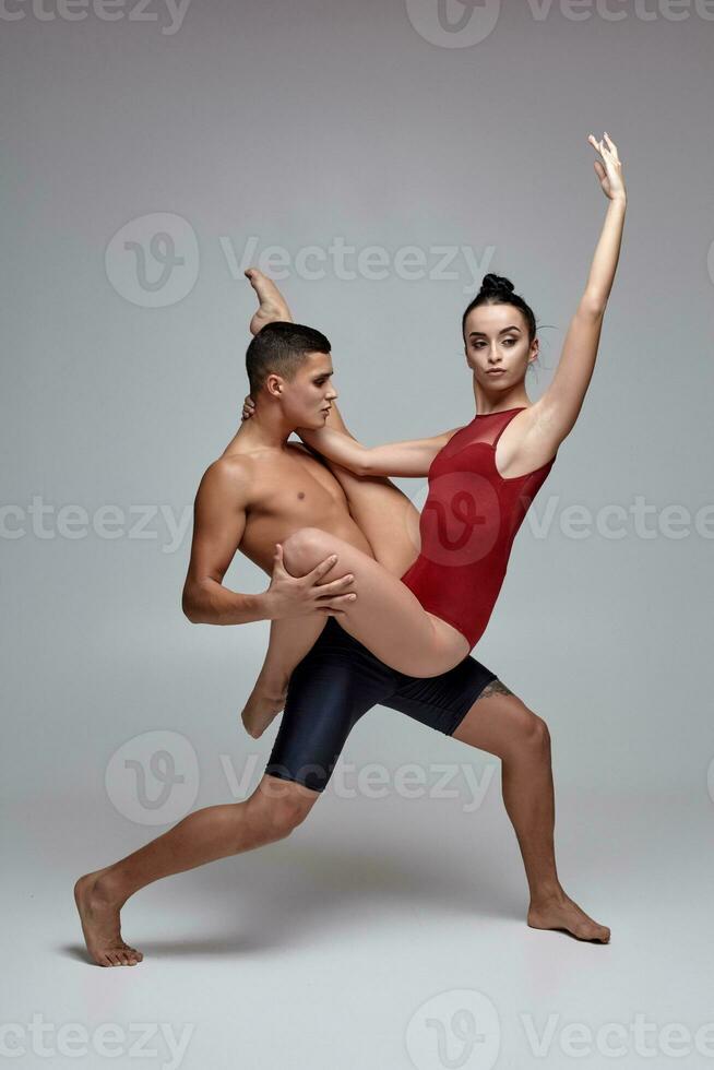 de paar van een atletisch modern ballet dansers zijn poseren tegen een grijs studio achtergrond. foto