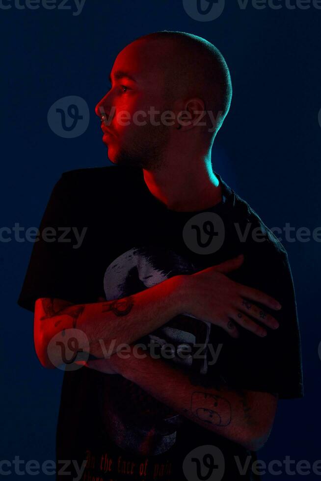 studio schot van een jong getatoeëerd kaal Mens poseren tegen een blauw achtergrond. 90s stijl. foto