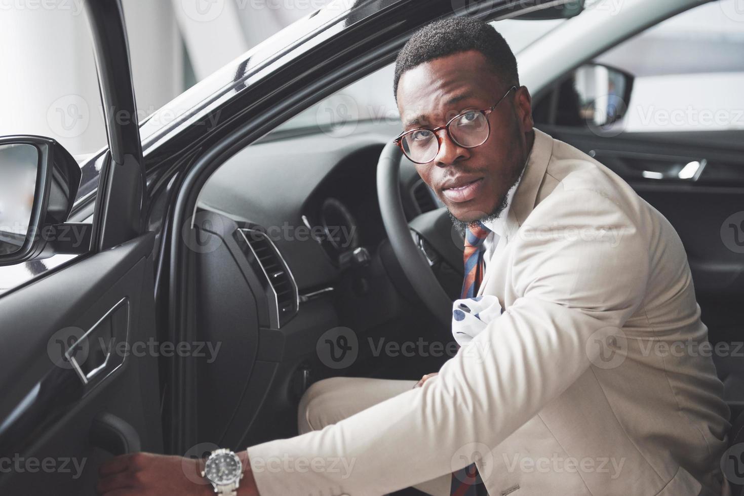 stijlvolle zwarte zakenman zit achter het stuur van nieuwe luxeauto. rijke afro-amerikaanse man foto