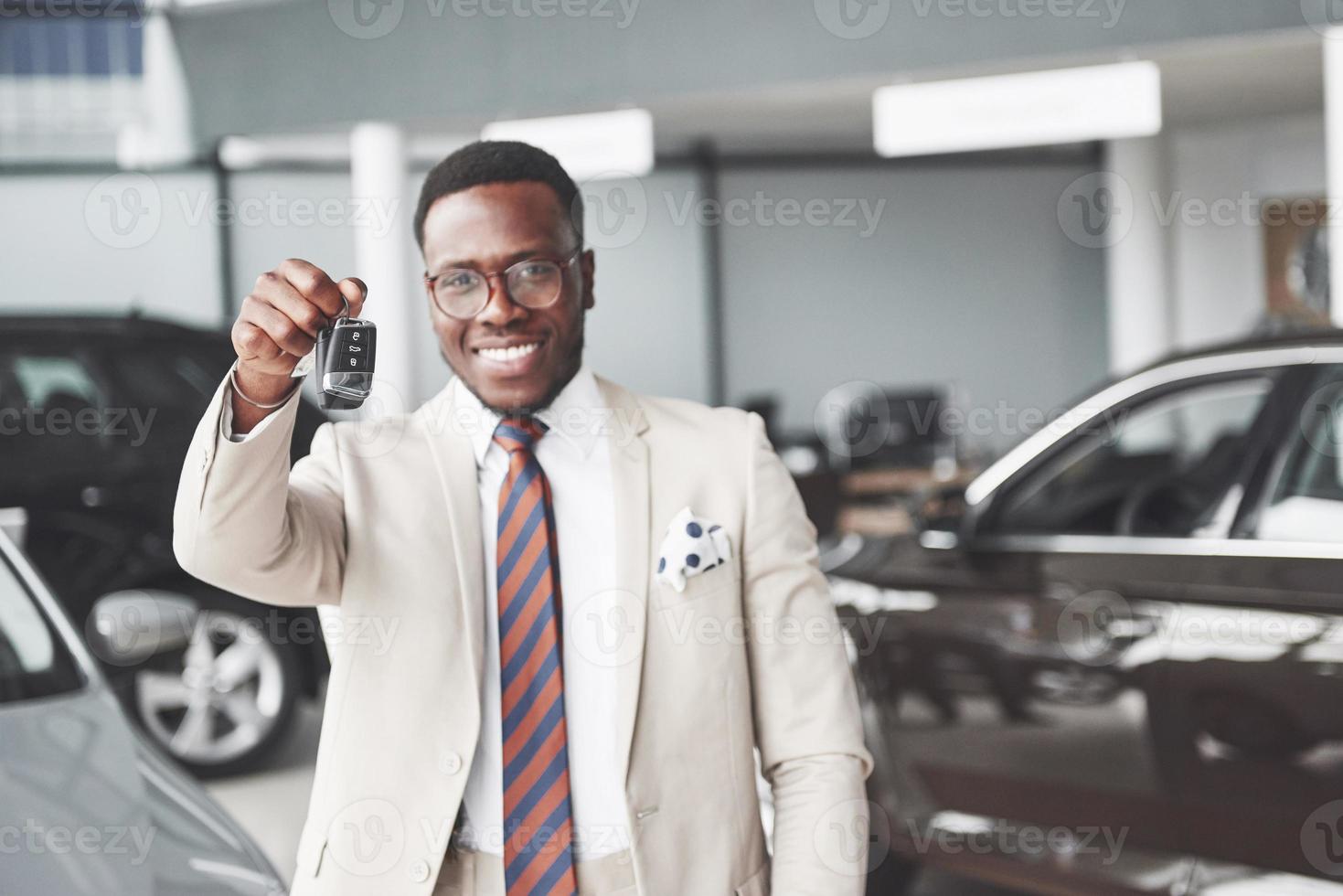 de jonge aantrekkelijke zwarte zakenman koopt een nieuwe auto, hij houdt de sleutels in zijn hand. dromen komen uit foto