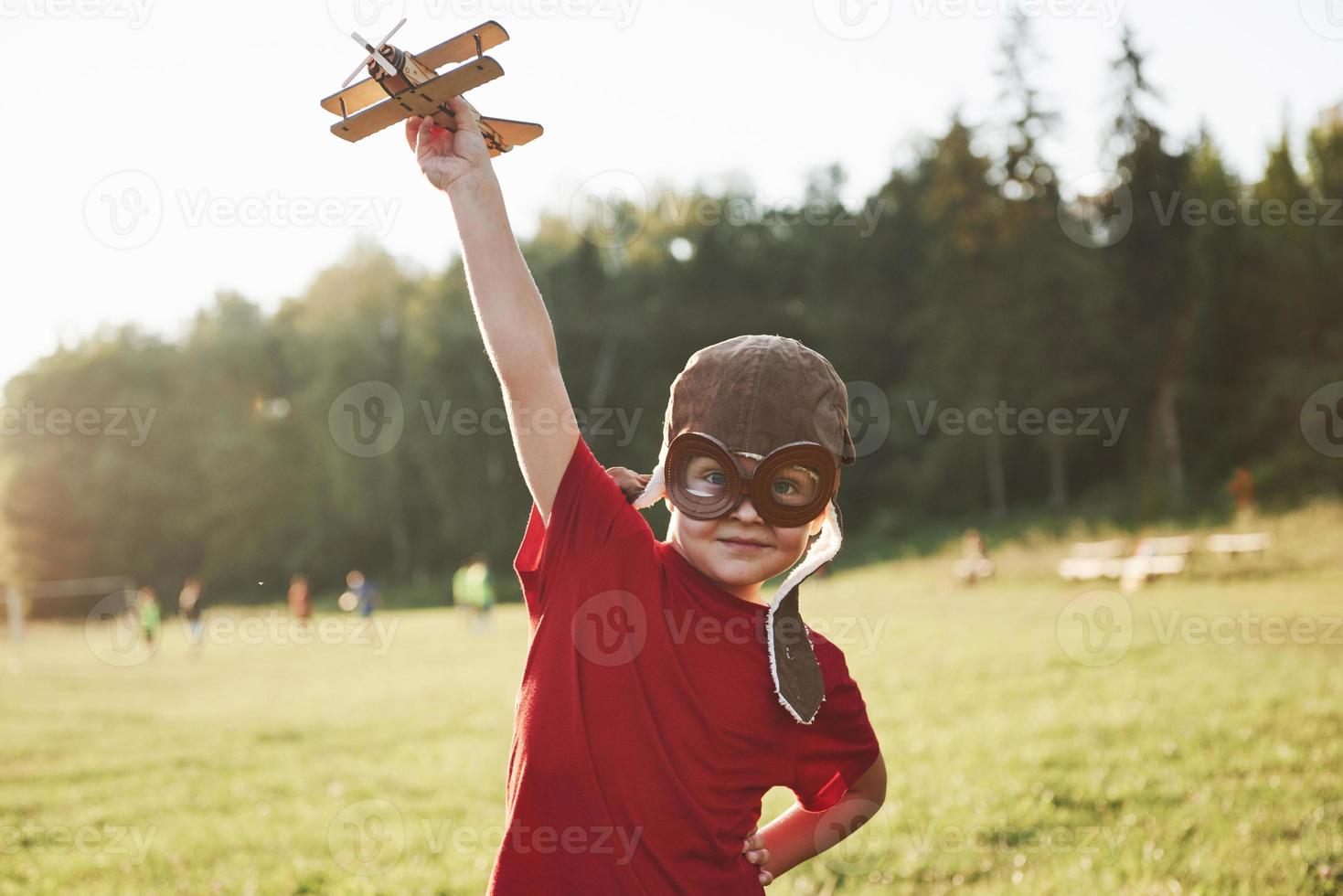 gelukkig kind in piloothelm speelt met een houten speelgoedvliegtuig en droomt ervan te kunnen vliegen foto