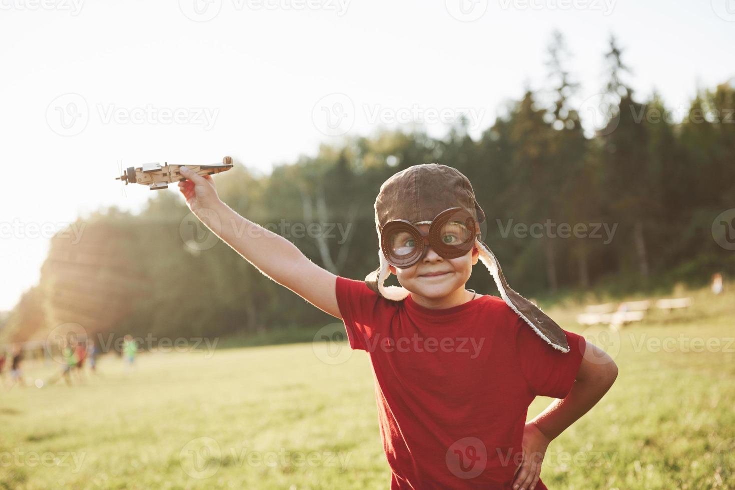 gelukkig kind in piloothelm speelt met een houten speelgoedvliegtuig en droomt ervan te kunnen vliegen foto