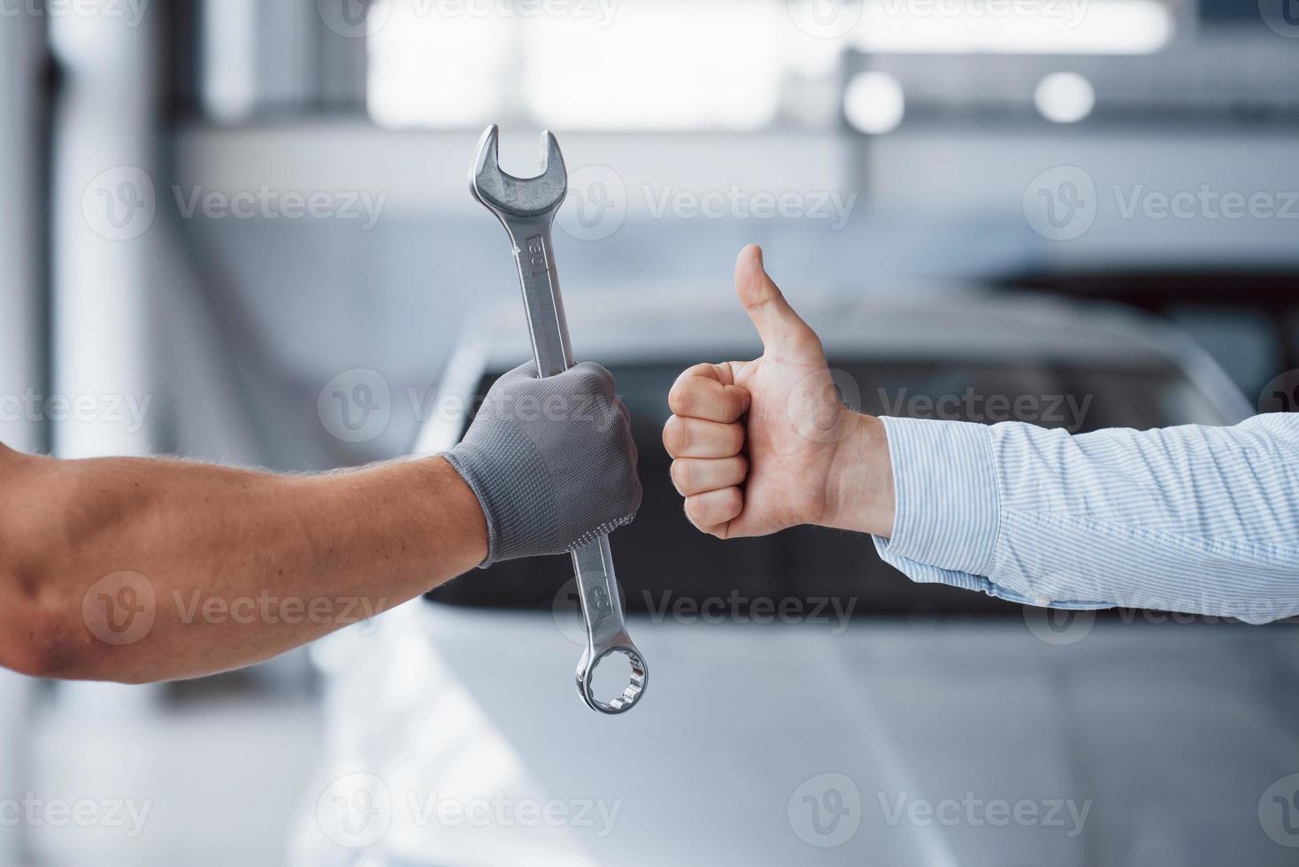 de automonteur houdt de sleutel in de hand van de klant en heft zijn duim op. goed gedaan werk foto
